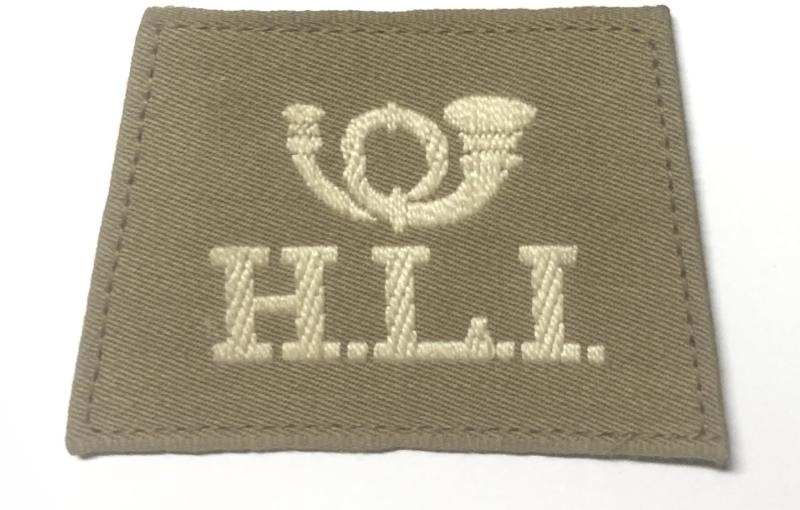 Good very scarce white embroidered coiled bugle over H.L.I. on light khaki material. Wide webbing tape fixing to reverse.
